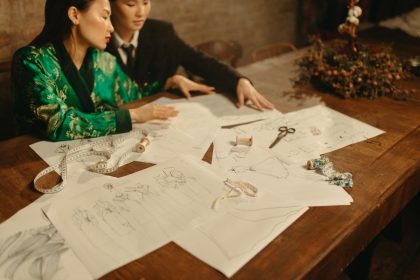 Dois designers trabalham em um projeto de moda cercados por esboços e ferramentas em um estúdio.