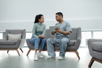 Profissional de saúde orienta uma paciente durante consulta, utilizando um tablet em uma sala clínica.