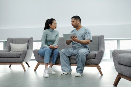 Profissional de saúde orienta uma paciente durante consulta, utilizando um tablet em uma sala clínica.
