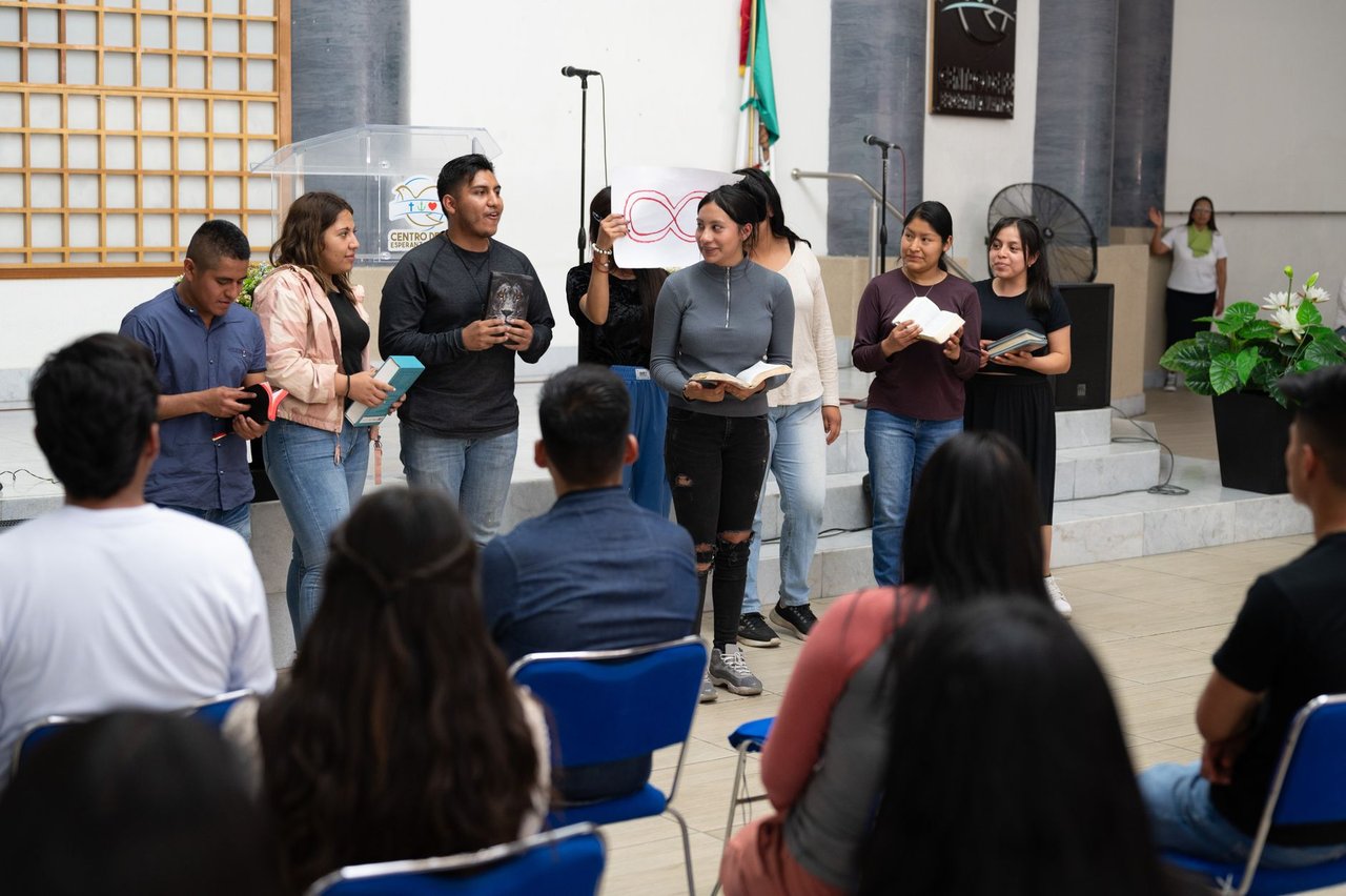 Jovens participam de uma atividade religiosa em uma igreja, acompanhando a celebração e fazendo leituras.