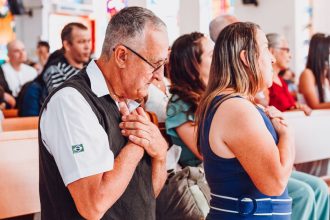 Grupo diverso de adultos reunido em uma igreja durante um momento de oração.