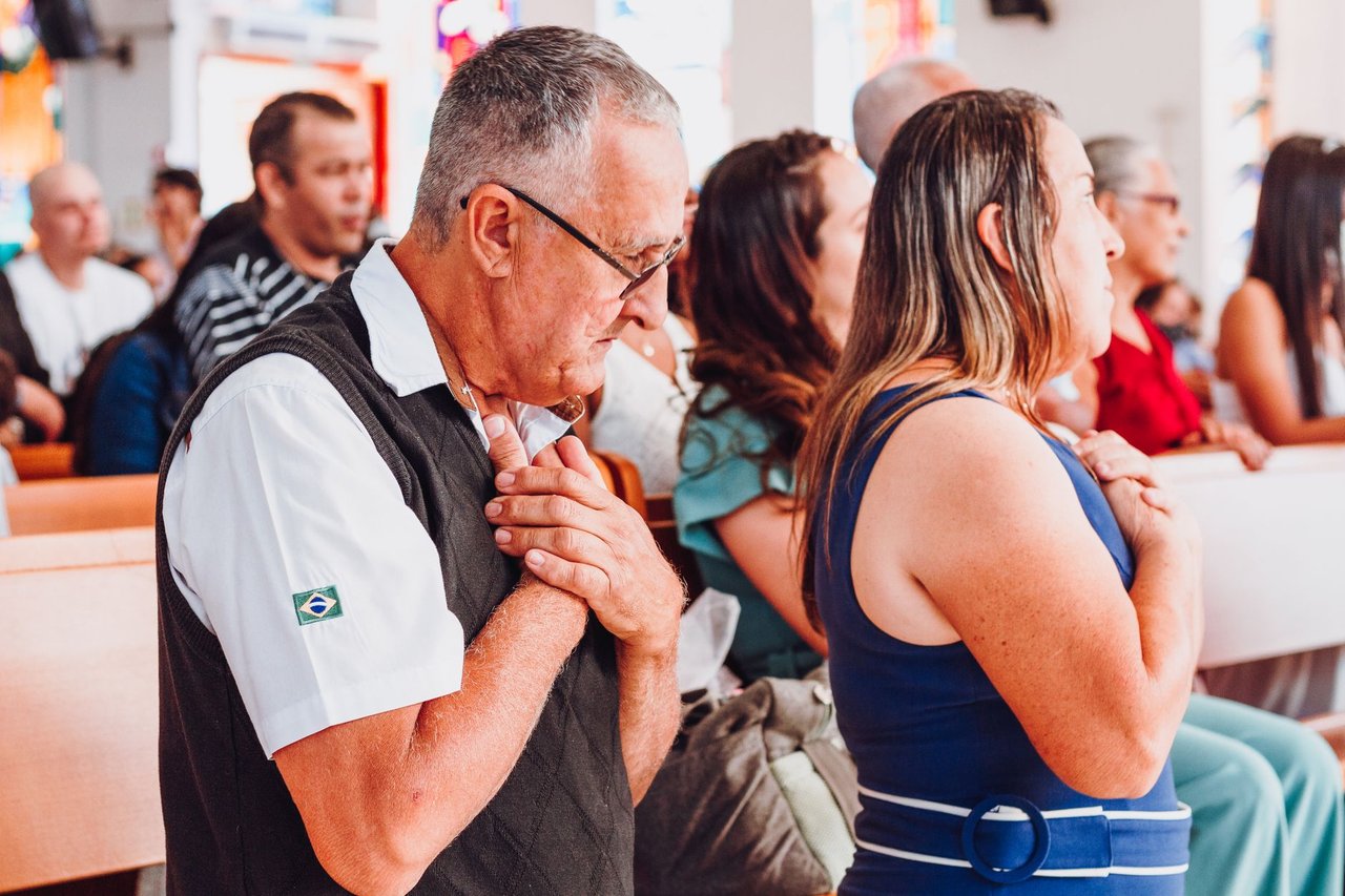 Grupo diverso de adultos reunido em uma igreja durante um momento de oração.