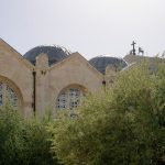 Igreja histórica em Jerusalém, cercada por oliveiras sob um céu claro.