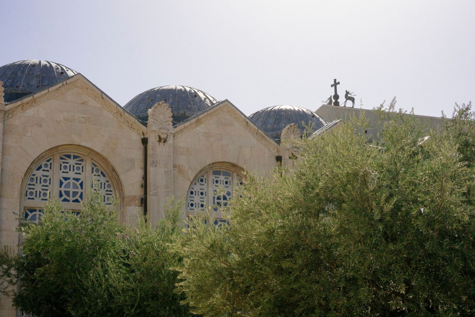 Igreja histórica em Jerusalém, cercada por oliveiras sob um céu claro.