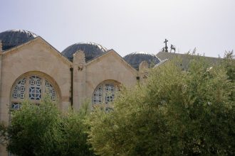 Igreja histórica em Jerusalém, cercada por oliveiras sob um céu claro.