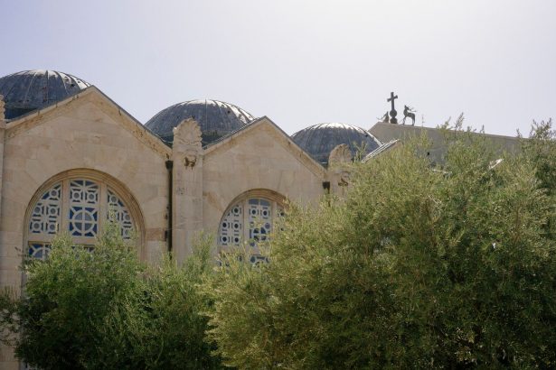 Igreja histórica em Jerusalém, cercada por oliveiras sob um céu claro.
